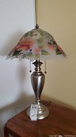 Full view of one table lamp showing floral glass shade and brushed silver base.