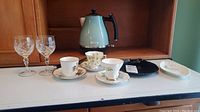 Overview photo of the lot with Royal Albert cups and saucers, Queen's cup and saucer, two dishes, Haden kettle and six crystal wine glasses.