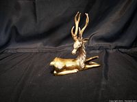 Photo of a brass reindeer figurine lying down against a dark fabric background