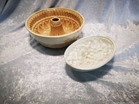 Photo of two ceramic pottery jelly moulds, one beige bundt-style and one white oval with fruit detail.