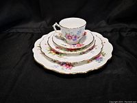 Stacked Aynsley china plates and cup with saucer showing floral pattern and gold trim