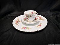 Three-piece china set including a cup, saucer, and dinner plate with floral Moss Rose pattern and gold trim on black background