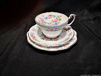 Photo showing one tea cup stacked on its matching saucer with the dessert plate underneath, highlighting the floral pattern of pink and blue flowers with green leaves and gold trim on Foley bone china.