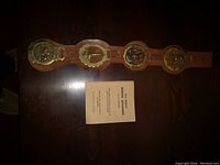 Photo showing four brass horse brasses mounted on a brown leather strap laid out horizontally next to a small booklet titled 'All About Horse Brasses'.