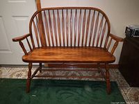 Wooden bench with vertical slat backrest, armrests, turned legs, and foam cushion on seat.