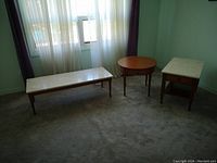 Photo of three wooden tables: one long rectangular coffee table with white marble top, one rectangular wooden end table with marble top and shelf, and one round wooden end table with decorative motif beneath top.