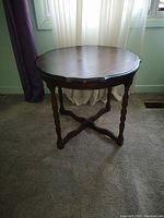 Photo of a round dark wood end table with scalloped edge top and X-shaped crossbar support base.