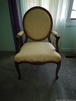 Front view of wooden armchair with yellow patterned tapestry fabric upholstery and carved legs.