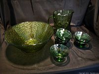 Photo showing large green glass bowl, green pitcher, and four smaller green glass bowls on a dark background.