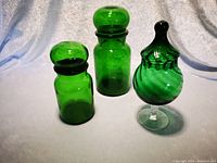 Photo showing medium and small bright green glass canisters with push-in lids alongside a green glass footed candy dish with rounded stopper lid and swirl texture.