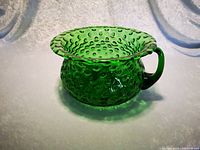 Side view showing the green glass bowl with a flared rim, handle on one side, and hobnail bubble texture all over the rounded body.