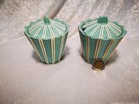 Two teal and white ceramic condiment pots with lids shown together with a coin for size reference.