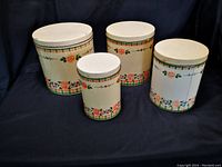 Front view of four vintage metal canisters, cream with pink and orange rose floral pattern, all with lids.