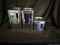 Photo of three vintage chrome canisters labeled S, C, and F against dark background.
