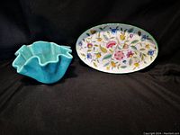 Photograph showing a teal fluted ceramic dish and a small oval porcelain tray with colorful floral design on black background.