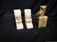 Photo showing three carved onyx bookends: two Aztec style human figures and one owl on onyx base, all visible details of carvings and stone patterning.
