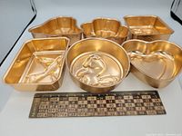 Photo of six copper-colored aluminum jelly moulds arranged with a wooden ruler for size reference.