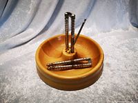 Single photo showing a round light brown wooden nut tray with a divided surface and central vertical holder, containing two silver-colored nut picks, along with two silver-colored nutcrackers placed on the tray.