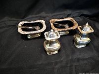 Two sets of silver salt cellars with blue glass inserts and matching silver spoons, alongside two silver pepper shakers with hinged lids.