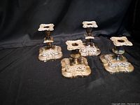 Photo showing two sets of silver candlesticks: one set has four candlesticks and the other has five. Each candlestick features a square base with intricate ornamental designs.