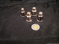 Four sterling silver salt and pepper shakers displayed on black fabric with a coin for scale.