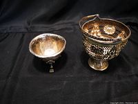 Photo showing a small silver footed dish with three lion paw feet beside a small silver handled plant pot with floral latticework design.