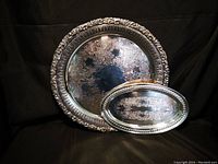 Two large silver serving trays, one round and one oval, shown side by side on black background