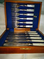 Wooden hinged box interior with blue felt showing six dinner forks above and six dinner knives below