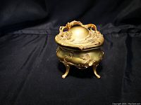 Front view of vintage cast metal jewelry casket with floral relief detailing and tripod legs