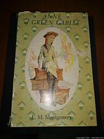 Front view of vintage hardcover book Anne of Green Gables featuring illustrated dust jacket with girl in braids and green patterned background.