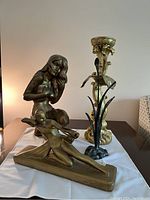 Three vintage gold-colored decorative items on a table: two statues and one ornate candle holder, photographed from the front.