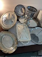 Full view of the collection showing multiple silver platters, covered dishes, a two-tiered stand, and an urn-style piece on a table.