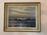 Frontal image of framed original oil painting depicting ocean waves with a colorful cloudy sky.