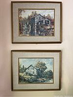 Photo of two framed farmhouse paintings hung vertically on a wall with beige fabric mats and gold frames.