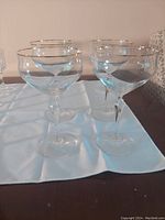 Four clear wine glasses with gold rim placed on a white cloth on a table.