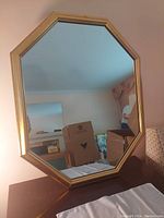 Full view of octagonal wall mirror with gold frame showing reflection of a room with boxes and furniture.