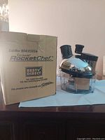 Photo showing the Culinare Rocket Chef food processor beside its original cardboard box on a surface.