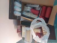 Three open boxes filled with various types, sizes, and colors of candles including taper, pillar, and votive styles. Some candles are still in plastic packaging indicating they are new.