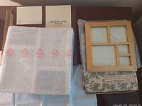 Photo of assorted picture frames in original packaging: silver plated frame wrapped in bubble wrap, wooden four-photo frame, and floral boxed frame.