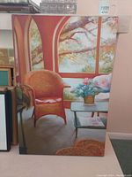 Photo of a 24x36 inch print on canvas showing a garden-themed scene indoors with an orange wicker chair and a flower on a table near arched windows.
