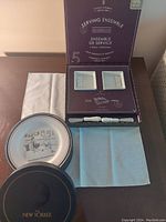 Photo showing two New Yorker illustrated plates, boxed serving ensemble containing two square serving dishes and two spreaders, and three cloth napkins in white, cream, and blue.