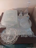Assorted clear glass platters, bowls, and two decanters arranged on a table.