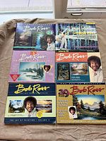 Photo of six Bob Ross painting instruction books showing colorful front covers with Bob Ross and landscape paintings.