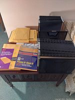 Photo displaying a collection of envelops and black accordion file organizers placed on a wooden table.