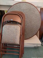 Photo of a 36 inch diameter round card table and four matching folding chairs, all with brown metal frames and beige/brown speckled laminate surfaces.