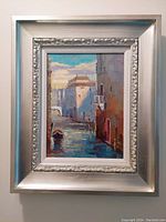 Framed oil painting depicting Venice canal with buildings and a boat, shown hanging on a wall.