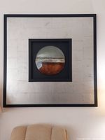 Frontal photo of large square metallic modern abstract art with a circular, horizontally striped central design in earthy and metallic tones.