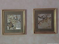 Photo of two framed gold leaf art pieces on a wall, showing floral and bird designs with gold leaf accents.
