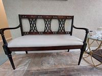 Front view of wooden bench showing full seat cushion and decorative armrests and legs.