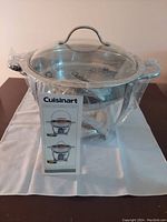 Photo of the Cuisinart brand new stainless steel chafing dish still in plastic wrap with clear glass lid on a stand, package tag attached.